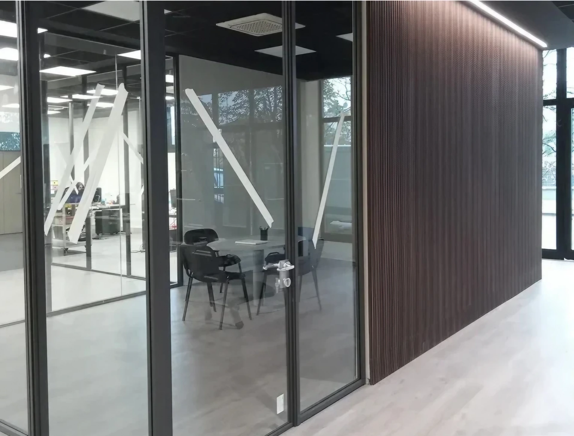 Interno ufficio moderno con pareti vetrate e divisori in legno, dopo interventi tecnici.