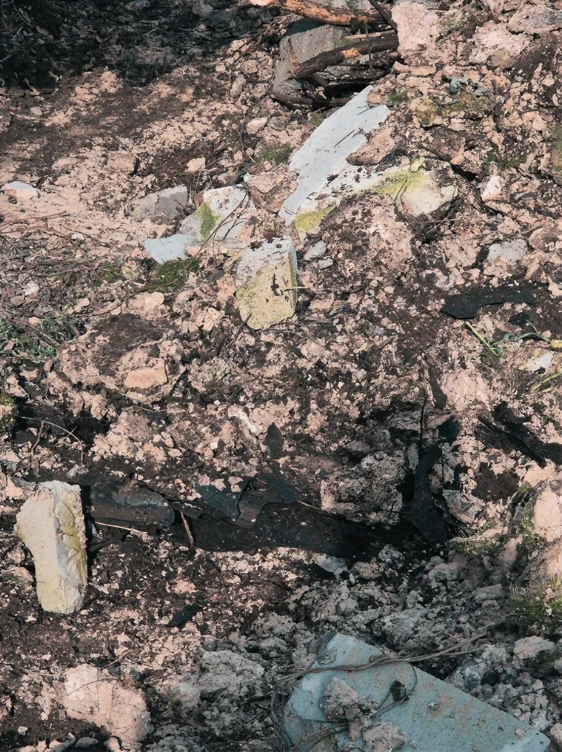 Cumulo di detriti edili misti a terra e materiali scuri, residuo di demolizione o bonifica cantiere.