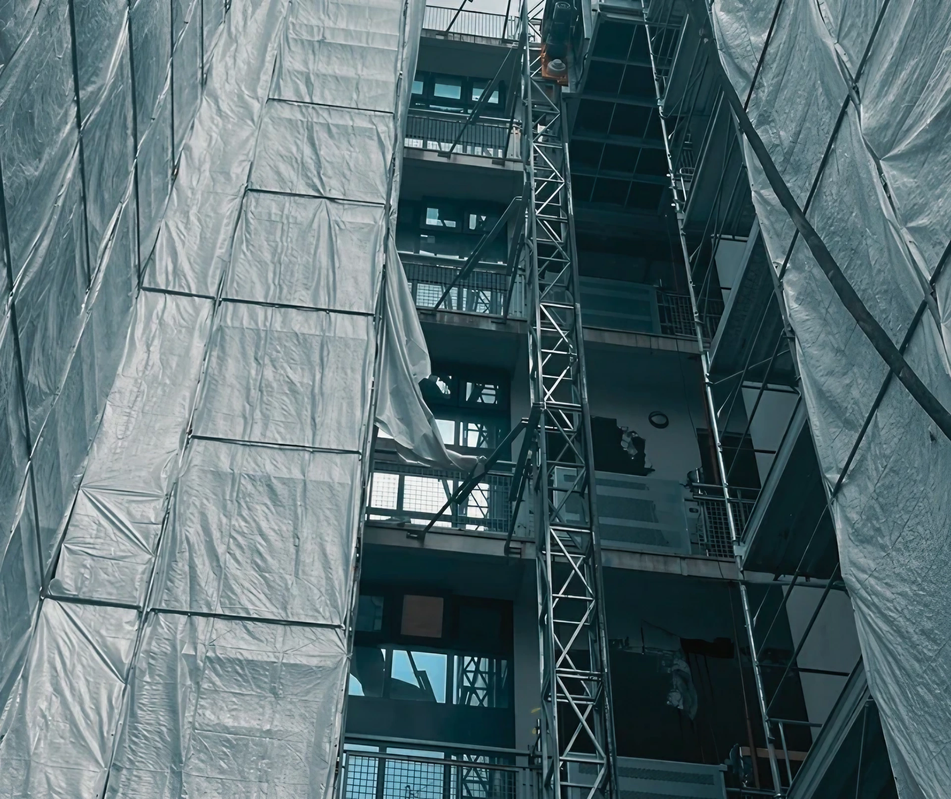 Edificio con ponteggi e teli protettivi, ascensore da cantiere. Preparazione per demolizioni.