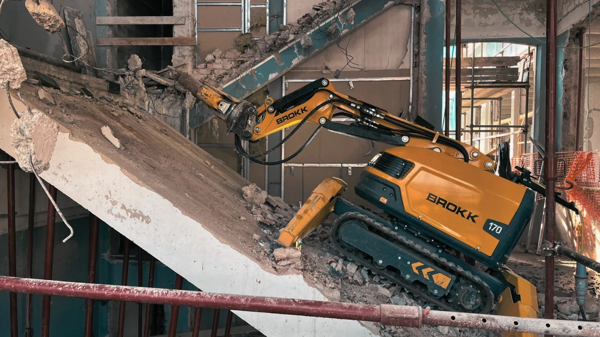 Robot Brokk 170 giallo in azione per demolizione controllata di struttura in cemento armato all'interno di un edificio.